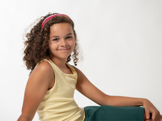 Wall Mural - Casual interracial school age girl with curly brown hair sitting isolated on white background