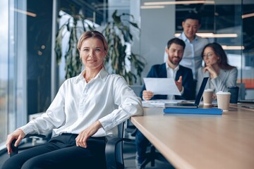 Wall Mural - Smiling confident female boss sitting on meeting in office with her colleagues at background. 