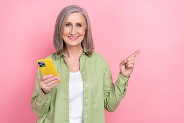 Sticker - Photo of woman gray hair pensioner hold new gadget iphone indicating empty space finger true information isolated on pink color background