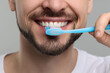 © New Africa - Man brushing his teeth with plastic toothbrush on light grey background, closeup