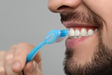 Wall Mural - Man brushing his teeth with plastic toothbrush on light grey background, closeup