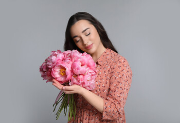 Poster - Beautiful young woman with bouquet of peonies on light grey background