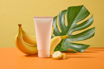 Wall Mural - An empty plastic bottle displayed with fresh bananas and green monsteras leaf on yellow background. Mockup for design, organic cosmetics, beauty products concept, banana extract