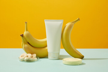 Wall Mural - An white tube decorated with ripe bananas, banana slices and cream on petri dishes on yellow background. Bananas have many wonderful uses for health and skin care. Minimal concept for advertising