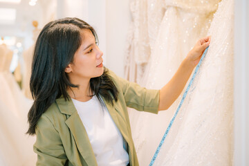 Portrait of entrepreneur bridal shop owner business woman fashion designer stylish working. Attractive designer girl using tape meter fitting on wedding dress with mannequin at wedding studio.