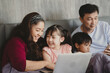 © chokniti - Happy Asian family lying on bed in bedroom with smile, father and mother with daughter and son, lovely parents using laptop computer for education and spent quality time together, laughing together