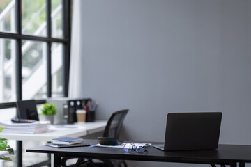 Wall Mural - Laptop Computer, notebook, and eyeglasses sitting on a desk in a large open plan office space after working hours	