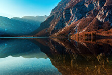 Beautiful Scenic Landscape, Rocky Mountain Hill Reflecting Of The Surface Of Clear Lake Bohinj In Slovenia In Winter
