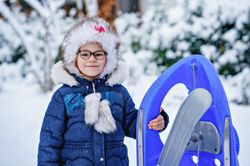 Wall Mural - Little girl enjoying a day out playing in the winter forest. Portrait of cute preschool child with glasses with sled. Kid having fun.