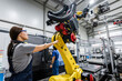 © Westend61 - Technician controlling robotic arm with colleague operating machinery in background