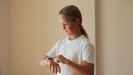 Portrait of pretty preteen girl using modern smart watch touching button and touchscreen while posing indoors on isolated background, touching button, setting smart watch. Shooting in slow motion.