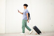 Full body side young man walking with mobile phone and travel bag