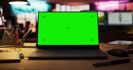 Leinwandbilder - Zoom Out of Mock-up Green Screen on a Laptop Standing on the top of a Wooden Table. In the Background Stylish Modern Office Studio in the Evening with Neon Lights. Desk of Creative Designer