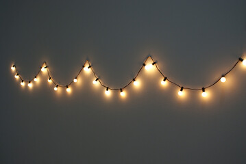 Yellow bulbs garland hanging on the grey wall indoors.