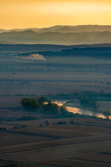 Wall Mural - Aerial view of the valley in early morning mist, beautiful in the highlands. Low clouds and fog cover the sleeping meadow. Alpine mountain valley mists landscape at dawn. Serene moment in rural area