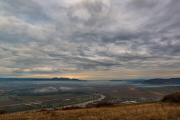 Wall Mural - Serene moment in rural area in beautiful early morning mist. Panoramic view of a sleeping meadow valley covered with low clouds and fog, a highway crossing a river, rolling hills and villages