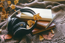 Audiobook Or Podcast In Fall Season. Wireless Headphones With Books And Autumn Leaves On Knitted Plaid As Concept Of Learning And Education, Online Courses Or Music App In Cozy Fall Mood.