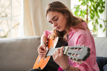 Wall Mural - Female musician feeling involved while playing acoustic guitar at home at her room