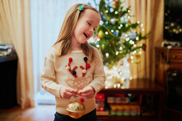 Wall Mural - Adorable little preschooler girl wearing holiday sweater decorating Christmas tree