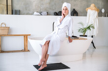 Young Woman In White Bathrobe Sitting On Edge Of Bathtub