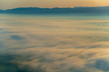 Wall Mural - Aerial view of the valley in early morning mist, beautiful in the highlands. Low clouds and fog cover the sleeping meadow. Alpine mountain valley mists landscape at dawn. Serene moment in rural area