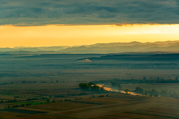 Wall Mural - Aerial view of the valley in early morning mist, beautiful in the highlands. Low clouds and fog cover the sleeping meadow. Alpine mountain valley mists landscape at dawn. Serene moment in rural area