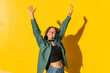 © VISTA by Westend61 - Carefree woman with arms raised in front of yellow wall