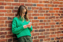 Teenage Girl Using Smart Phone Leaning On Brick Wall