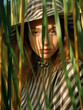 © GVS - Pretty young woman in a striped dress and hat peeking out from the tall green grass