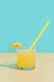 Fototapeta Tęcza - Tangerine juice in a glass with slice and straw. Turquoise and beige background. Minimalism.