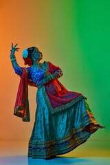 Wall Mural - Indian culture. Mature, beautiful indian woman in traditional clothes, dress posing over gradient studio background in neon light. Concept of beauty, fashion, India, traditions, choreography, art. Ad