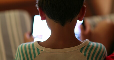 Boy staring at screen at night. back of Child watching content online