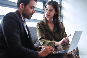 Young businesswoman talking with boss while pointing at laptop computer display in modern office.