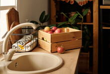 Beige Metallic Tap And Sink On Kitchen Counter With Wooden Box Of Ripe Apples Grown In The Garden By Country House Or Cottage In Autumn