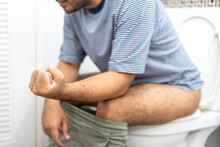 Man suffers from diarrhea having a stiff fist sitting on toilet bowl. Hand holding stomach with diarrhea excreting in toilet. Male is feeling pain with constipation.