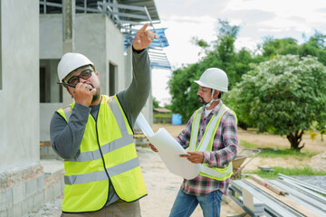 Asian construction supervisor Use a wireless radio Talk to high crane operator. to control crane Man standing using walkie-talkie at home construction site Wear helmet and reflective safety equipment.