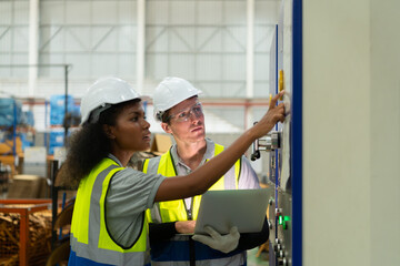 Portrait of two female engineers using laptop while standing in factory, To check the operation of the machine's circuit board.