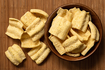 Wall Mural - Lentil chips in a rustic wood bowl next to a pile of lentil chips on bamboo matt from above.