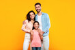 © Prostock-studio - Happy european family of three hugging and smiling to camera, posing together over yellow studio background