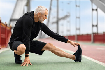 Athletic elderly sportsman strecthing legs, have outdoor workout