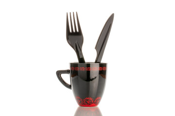 Wall Mural - One plastic knife and fork in a black ceramic cup, macro, isolated on white background.