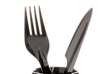 Wall Mural - One plastic knife and fork in a black ceramic cup, macro, isolated on white background.