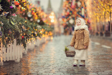 Little Russian Girl Wearing Shawl And Fur Coat On Christmas Market With Lights On Background 