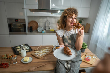 Wall Mural - One adult caucasian woman stand in the kitchen with fresh croissant