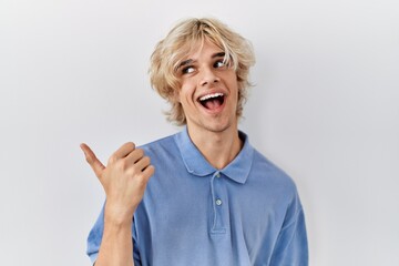 Canvas Print - Young modern man standing over isolated background smiling with happy face looking and pointing to the side with thumb up.