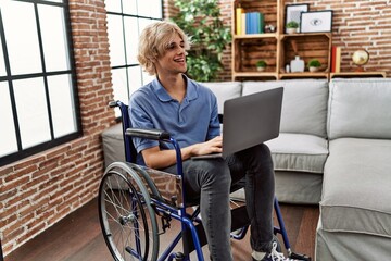 Sticker - Young blond man using laptop sitting on wheelchair at home