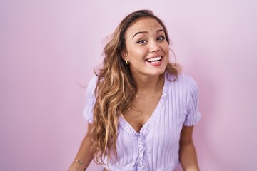 Wall Mural - Young hispanic woman standing over pink background smiling cheerful with open arms as friendly welcome, positive and confident greetings