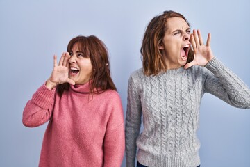 Sticker - Mother and daughter standing over blue background shouting and screaming loud to side with hand on mouth. communication concept.