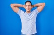 Young hispanic man standing over blue background relaxing and stretching, arms and hands behind head and neck smiling happy