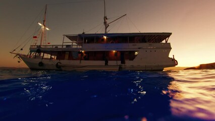 Wall Mural - Liveaboard boat anchored in the bay. Splitted underwater view during sunset. The Komodo National Park, Indonesia